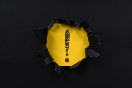 black torn paper revealing exclamation mark on yellow paper. exclamation mark background concept.の写真素材