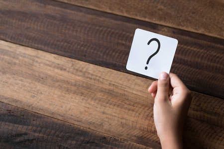 hand holding a note written a question mark on a wooden table backgroundの写真素材