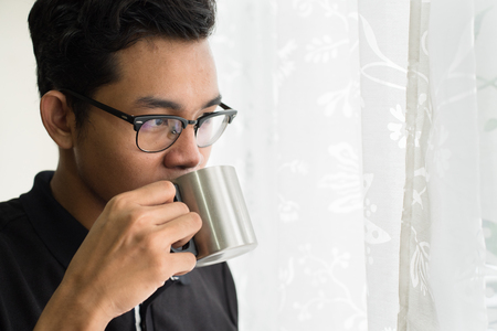 asian teenage sipping hot drinks while looking out of windowの写真素材