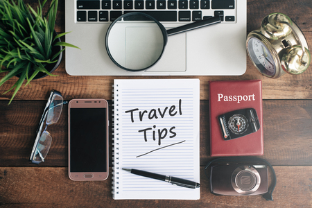 laptop, notebook, smartphone, passport, compass, magnifying glass and clock with TRAVEL TIPS word on wooden table. travel conceptの写真素材