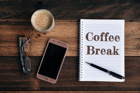 phone, glasses, coffe mug and notebook with COFFEE BREAK word on wooden table. coffee break conceptualの写真素材