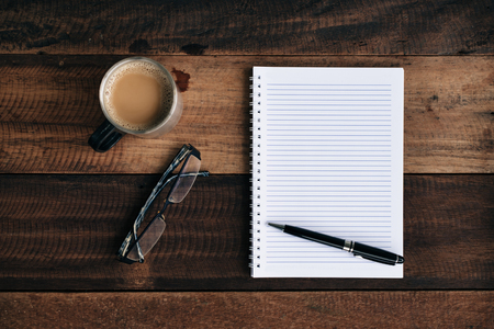 coffee, glasses pen and empty notebook on wooden table. flat lay top viewの写真素材