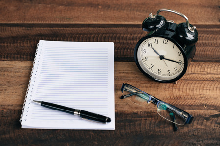 Clock, glasses, pen and blank notebook on a wooden table backgroundの写真素材