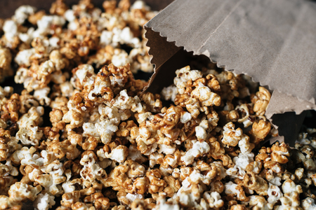 fresh caramel popcorn in a paper bag on wooden tableの写真素材