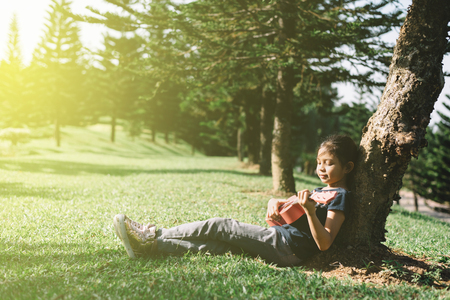young and happy asian girl playing with ukelele guitar at the park in sunny morning. hobbies and tranquility conceptの写真素材