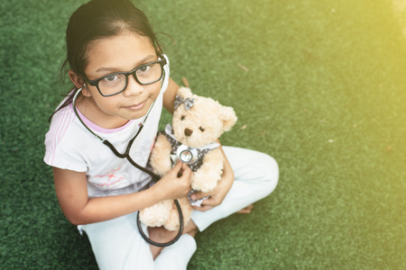 young little asian girl playing pretend to be a doctor. young girl eaxamine her teddy bear with stethoscope. ambition and child healthcare conceptの写真素材