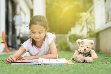 younf asian girl reading a book lying on her house lawn. child education conceptの写真素材