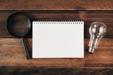 magnifying glass, bulb and blank notebook on wooden table. research and idea conceptの写真素材