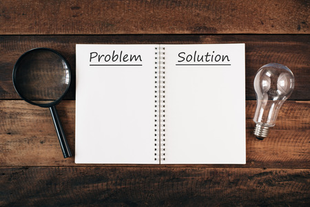 magnifying glass, bulb and notebook written PROBLEM and SOLUTION with copy space on wooden table. problem solving conceptの写真素材