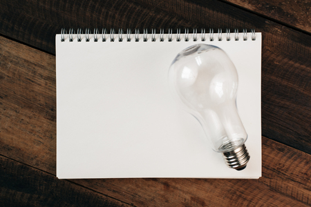 light bulb on a blank book on a wooden table. idea and energy saving conceptの写真素材