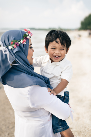 loving young asian mother holding her son smiling and laughing at the beach. family conceptの写真素材