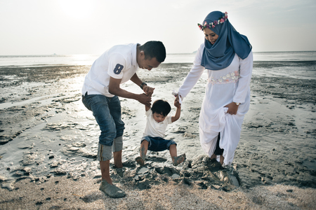 happy asian family wearing casual and playing with mud at the muddy beach located in pantai remis, kuala selangor, selangor, malaysiaの写真素材