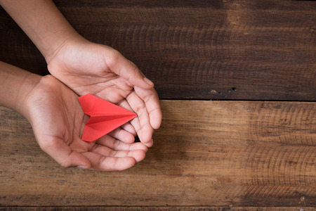 hand showing or holding red paper airplane on wooden table background. freedom and childhood conceptの写真素材