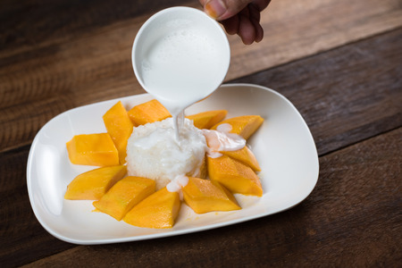 pouring cocunut milk onto mango sticky rice, a traditional thailand dessert. food and gastronomy conceptの写真素材