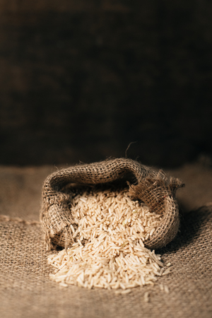 vertical image of a natural unpolished brown rice in burlap sack over dark background. healthy food and eating conceptの写真素材
