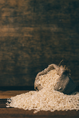 vertical image of natural brown rice in burlap sack on wooden table. healthy food and eating conceptの写真素材