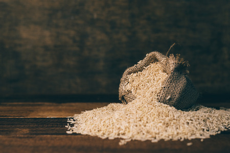 Natural unpolished brown rice in a small burlap sack on wooden table over dark background. healthy food and eating concept. selective focusの写真素材
