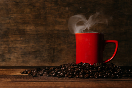red mug with steam on a pile of fresh roasted coffee beans over wooden table. coffee break and beverage conceptの写真素材