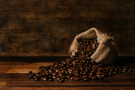 bunch of fresh roasted coffee beans with burlap sack on a wooden table. agriculture and drink conceptの写真素材