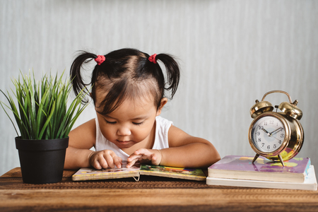 cute little asian toddler reading a book on a wooden table. concept of child early education, child growth and developmentの写真素材