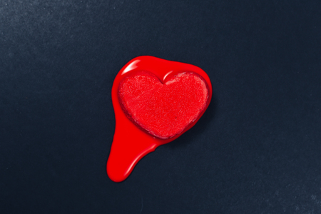 red heart shape ice cream melting on dark or black textured paper background. concept of love, emotions, feelings and heart cardiology health careの写真素材
