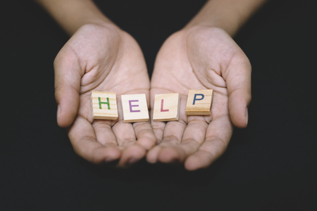 wooden alphabet tiles word HELP in a child hand over dark background. concept of help, charity and...