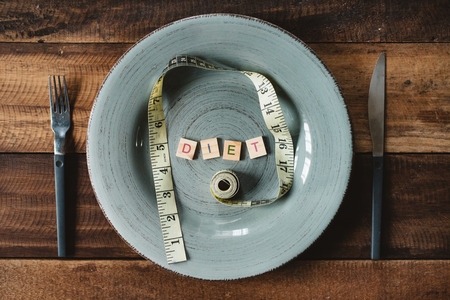 Measuring tape and word DIET in a plateon a wooden table. concept of dieting and weight managementの写真素材