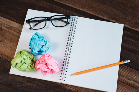 Eyeglasses, crumpled paper and blank spiral notebook with copy space on a wooden table. Concept of school, writing, sketching and workspace.の写真素材