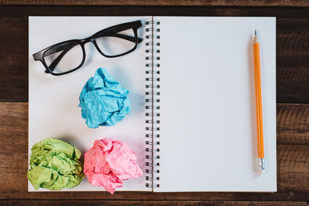 Eyeglasses, crumpled paper and blank spiral notebook with copy space on a wooden table. Concept of school, writing, sketching and workspace.の写真素材
