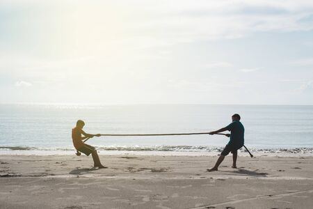 two asian kids pulling a rope at the beach. concept of friendship and competitionの写真素材