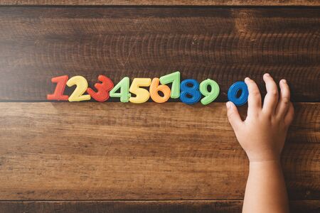 Child hand holding number zero with sets of other colorful numbers plastic toy on a wooden table. Concept of child learning numbers and child educationの写真素材