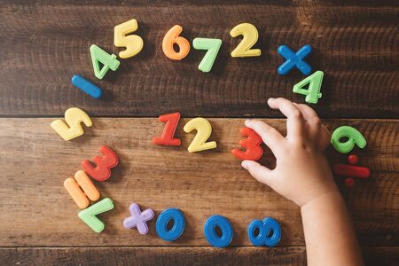child hand holding a colorful plastic toy numbers on a wooden table. children learning counting numbers 123. concept of early educationの写真素材