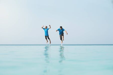 two young teenager jumping together into a overflow swimming pool. Concept of holidays, vacation, happiness and friends having funの写真素材