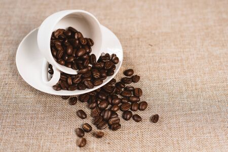 coffee beans overflow on a white cup over a burlap sack. concept of favorite drink and agricultureの写真素材