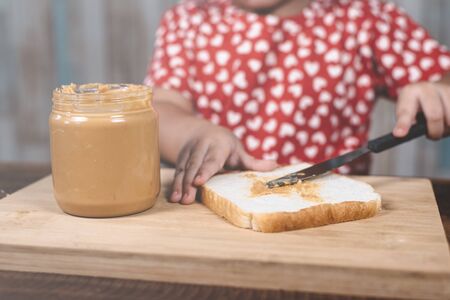 little asian girl spreading  a peanut butter on a white bread. Concept of peanut butter loverの写真素材