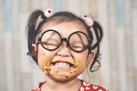 cute little girl with mouth smeared with peanut butter. Concept of penut butter loverの写真素材