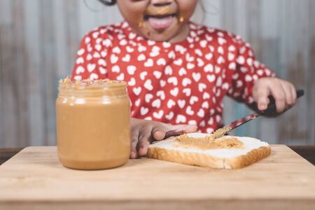 little asian girl spreading  a peanut butter on a white bread. Concept of peanut butter loverの写真素材