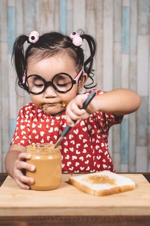 little asian girl spreading  a peanut butter on a white bread. Concept of peanut butter loverの写真素材