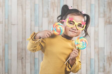 Cute little asian girl holding and eating a colorful lollipop. concept of oral care and candy dayの写真素材