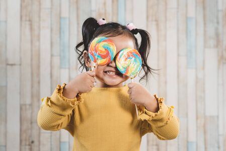 Cute little asian girl holding and eating a colorful lollipop. concept of oral care and candy dayの写真素材
