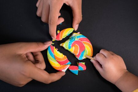 Child sharing lollipop on black background, concept of sharing,friendship,togetherness and teamworkの写真素材