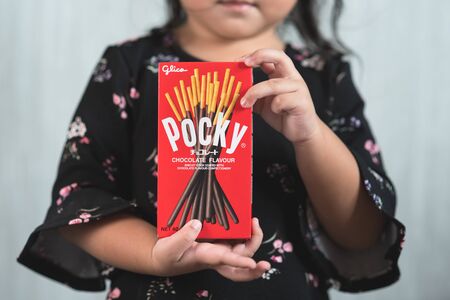 Petaling jaya, Selangor, Malaysia - 20 Oktober 2019 : Little asian girl holding a box of pocky brand of chocolate sticks. Pocky is a famous confectionery among asian peopleのeditorial素材