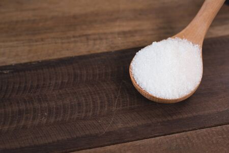 heap of white sugar in a wooden ladle over wooden table. concept of unhealthy eating and diabetesの写真素材