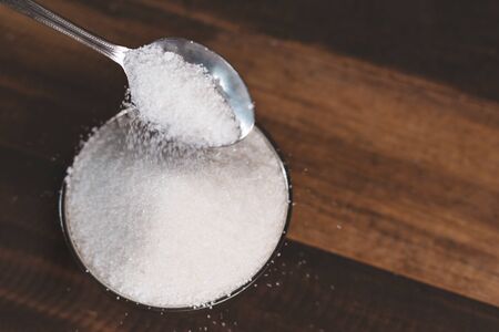 Sugar poured into a steel bowl on a wooden table. Concept of unhealthy eating and diabetesの写真素材