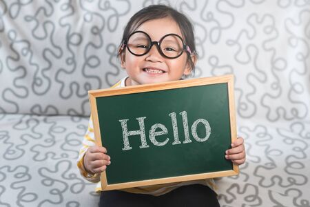 Little asian girl holding a chalkboard with a word HELLO. Concept of Hello day, Greetings, Introduction and lifestyleの写真素材