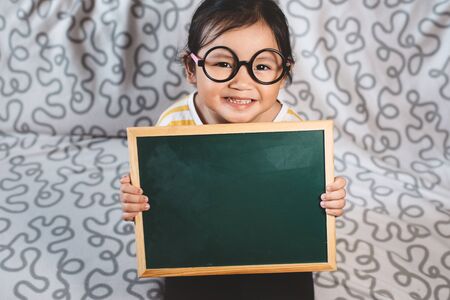 Little Asian girl holding blank chalkboard on her couch. concept of childhoodの写真素材