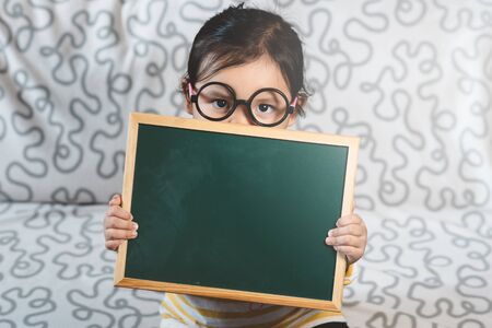 Shy little asian girl holding blank chalkboard. Concept of childhood, education and announcementの写真素材