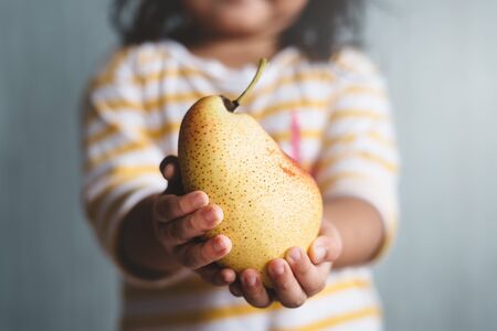little child holding a pear fruit in her hand with selective and shallow depth of field blurry...