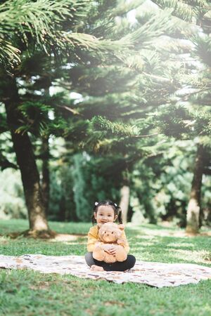 Little asian girl hugging her teddy bear in a park. Concept of happiness and childhoodの写真素材