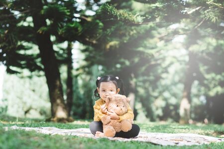 Little asian girl hugging her teddy bear in a park. Concept of happiness and childhoodの写真素材